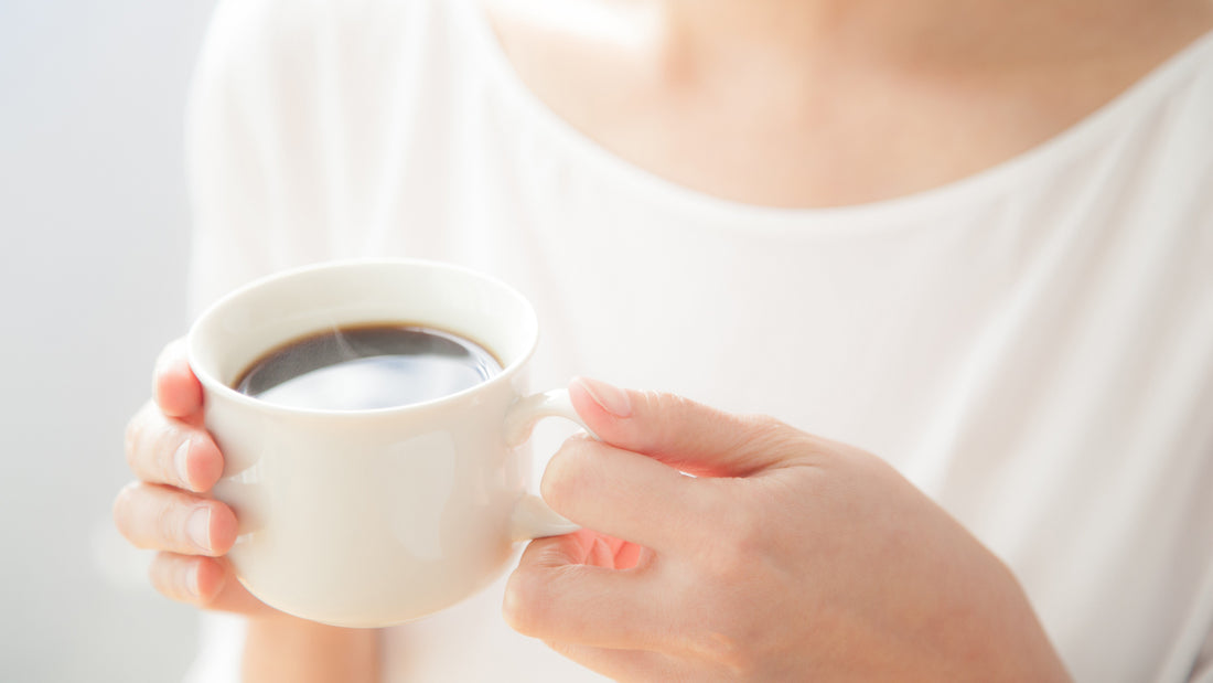 Woman holding white coffee cup with black coffee in bright, calm setting