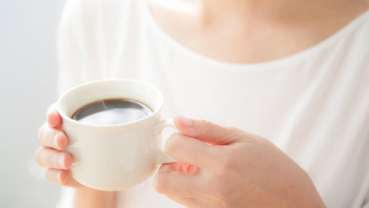 Woman holding white coffee cup with black coffee in bright, calm setting