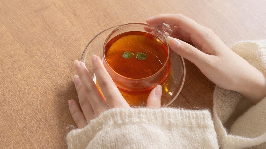 Hands holding a clear cup of herbal tea with mint leaves on a wooden table
