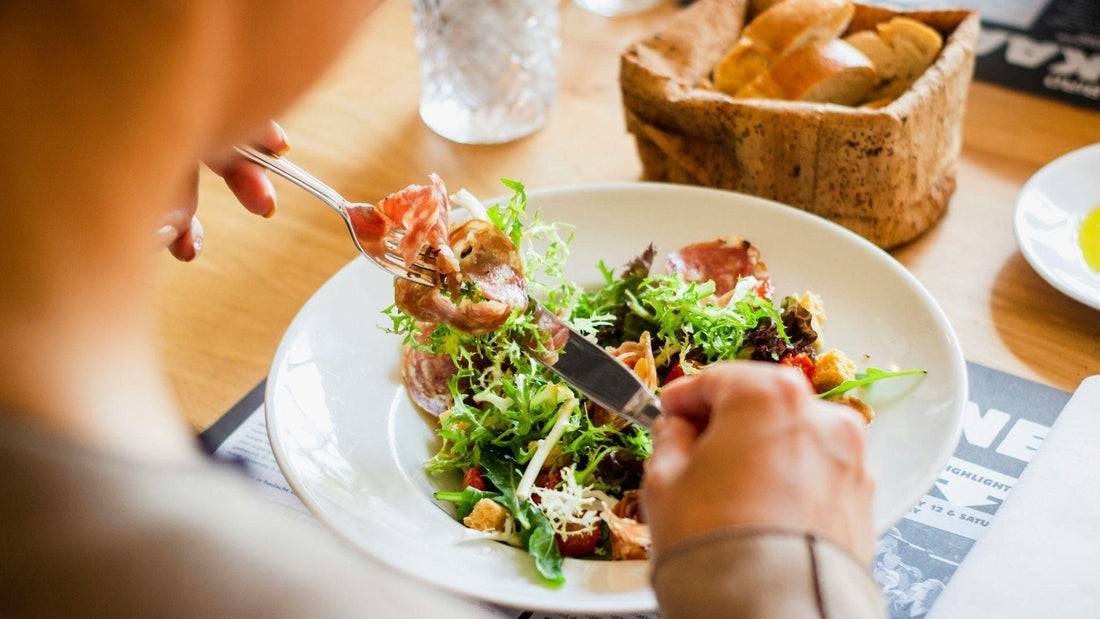 Person enjoying fresh salad with greens and cured meat at a restaurant table