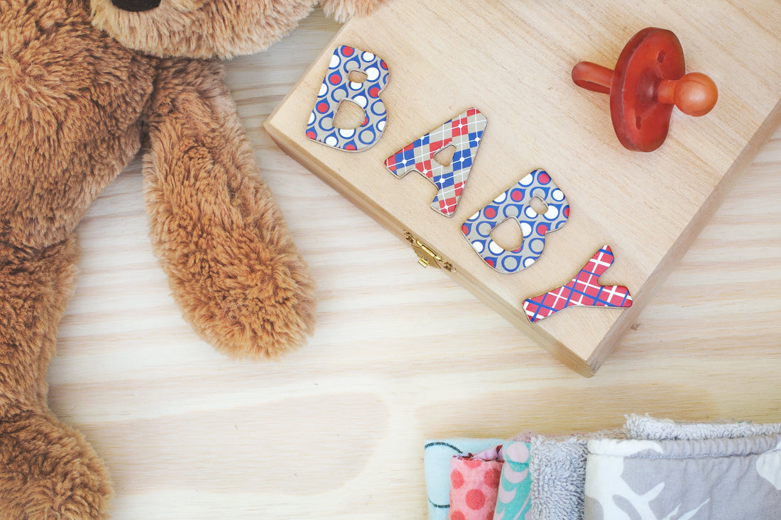 Baby nursery flat lay with teddy bear, pacifier, and colorful letters on wooden box