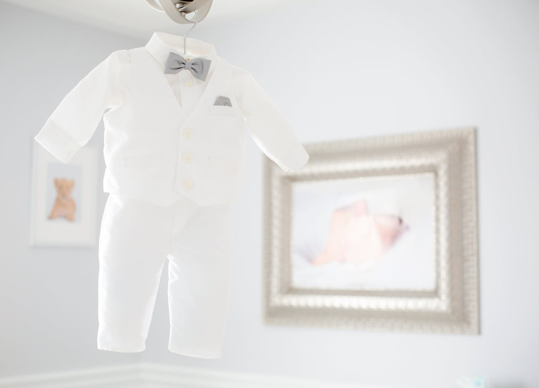 White baby tuxedo with grey bow tie hanging in a light nursery room