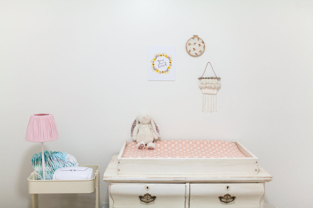 Minimalist baby nursery with changing table, stuffed bunny, diapers, and pink lamp