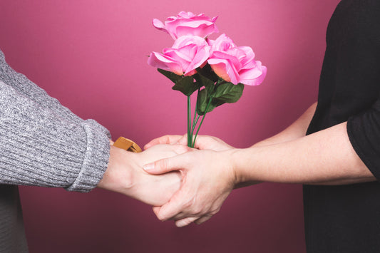 Couple holding hands and pink flowers against a pink background, symbolizing love and support.