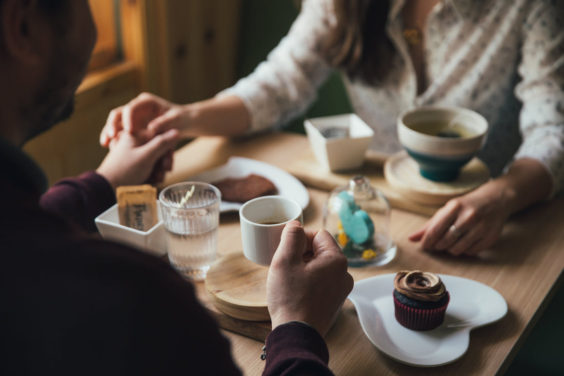 Couple holding hands at a cozy café table with coffee, cupcake, and pastries