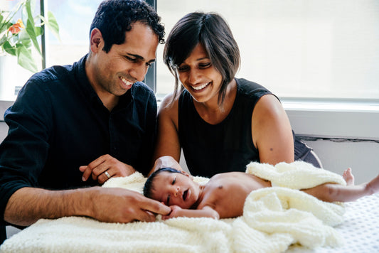 Happy couple smiling at newborn baby wrapped in a blanket, family bonding at home