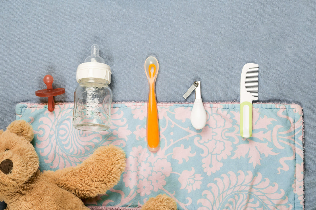 Newborn baby essentials including pacifier, bottle, spoon, nail clipper, comb, and teddy bear