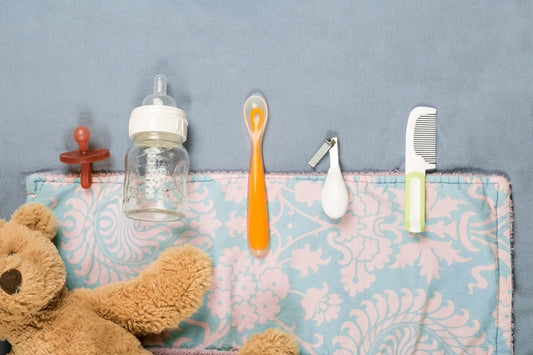 Newborn baby essentials including pacifier, bottle, spoon, nail clipper, comb, and teddy bear